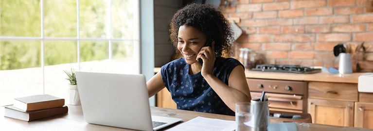 A woman seated at a table with a laptop, speaking on the phone, illustrating the concept of workplace flexibility.