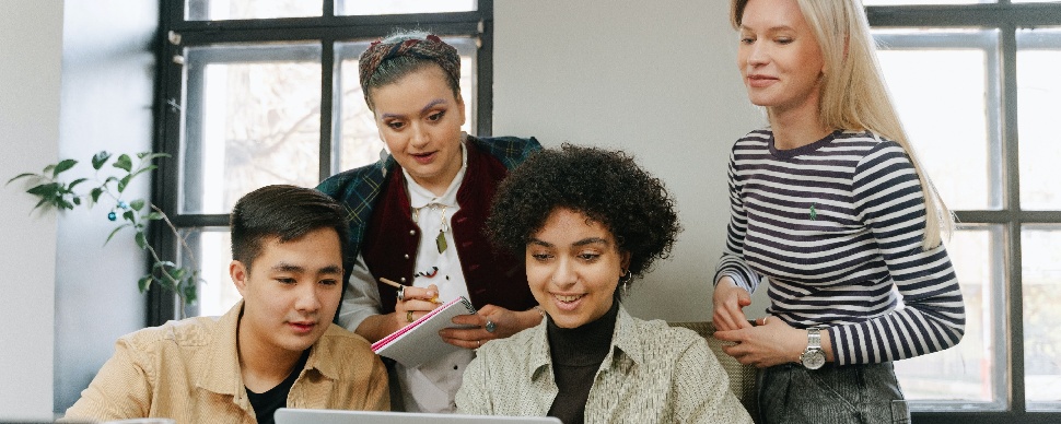 A gender-diverse group of young individuals focused on a laptop, working together on a project.