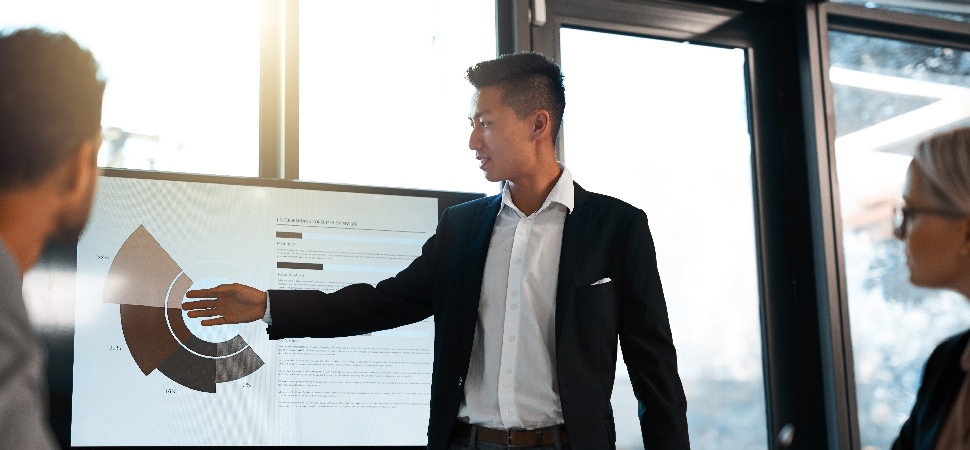 Three white-collar professionals looking at a graph on a screen in an office setting