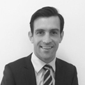 Black and white portrait of a smiling man in a suit with a striped tie.