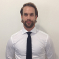 Man in a white shirt and black tie standing against a white background.