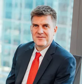 Man in a suit with a red tie sitting by a window with city view.