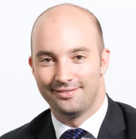 Portrait of a smiling man in a suit with a light background.