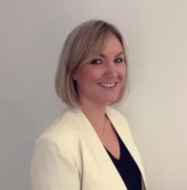 Portrait of a smiling woman with short blonde hair in a white blazer.