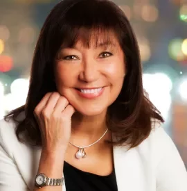 Smiling woman with dark hair and a necklace against a blurred colorful background.