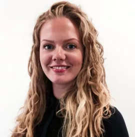 Smiling person with long curly hair, wearing a black top, against a plain background.