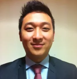 Smiling person in a suit and tie, against a plain background.