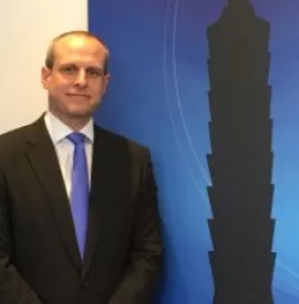 Man in suit with blue tie stands near silhouette of a tower.