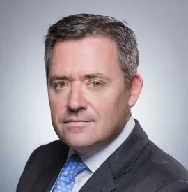 Man in a suit and blue tie against a gray background.