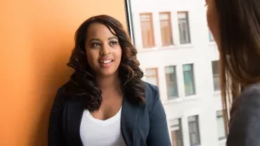 Two women having a conversation in an office setting.