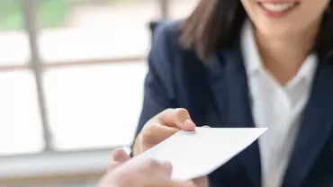 A woman hands over a business card with a smile.