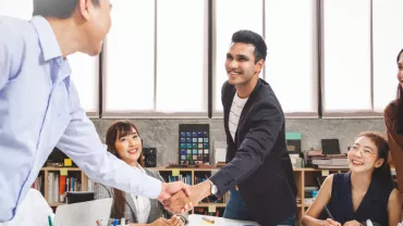 Colleagues in an office meeting, shaking hands and smiling.