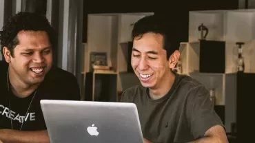 Two people smiling and looking at a laptop screen.