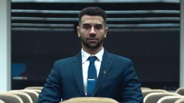 Man in a suit sitting alone in an empty lecture hall.