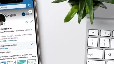 Smartphone showing a LinkedIn profile next to a keyboard and plant.