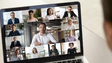 A person participating in a video conference with multiple people on a laptop screen.