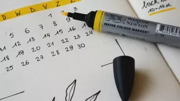 A pen next to a hand-drawn calendar on a notepad.