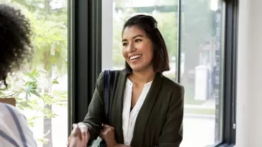Smiling woman in business attire shaking hands near a window.