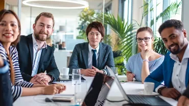 Diverse colleagues in a modern office meeting around a table.