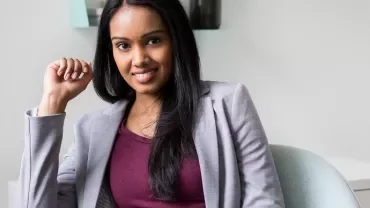 Smiling woman in a gray blazer sitting in a chair.