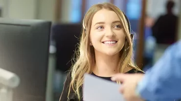 Smiling woman at her desk in an office setting, receiving a document.