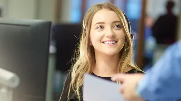 Smiling woman at her desk in an office setting, receiving a document.