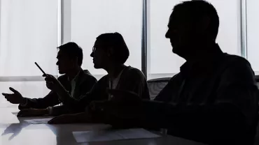 Silhouettes of three people sitting at a table during a discussion.