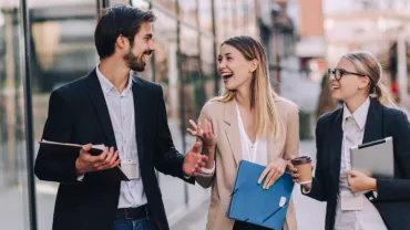 Three professionals walking and talking outside near office buildings.