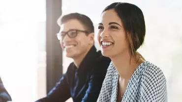 Two people smiling and sitting at a table in an office setting.