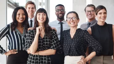 Group of eight professionals in business attire smiling in a modern office setting.