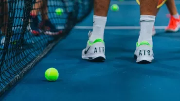 Tennis players on a blue court with tennis balls scattered around.