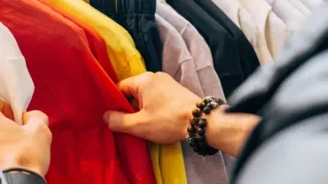 Person browsing colorful shirts on a clothing rack.