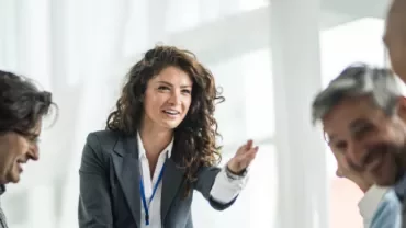 Woman in a suit speaking to a group during a meeting.