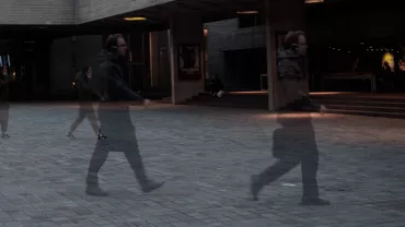 Blurred motion of people walking outside a theatre at night.