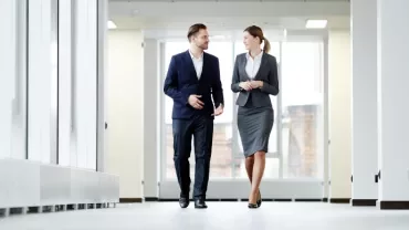 Two business professionals walking and talking in an office corridor.