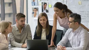 Group of professionals discussing a project around a laptop in a modern office.