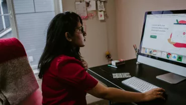 Woman in red top working on a computer at a home office.
