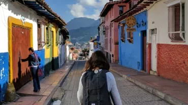 Person walking down a colorful street with mountains in the background.