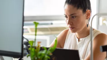 Woman concentrating on work at her desk with a computer and plant.