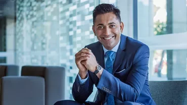 Smiling man in a blue suit sitting in a modern office setting.