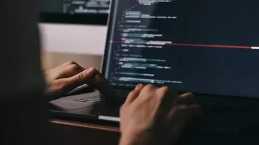Person typing code on a laptop in a dimly lit room.