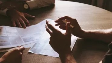 People discussing papers around a wooden table.