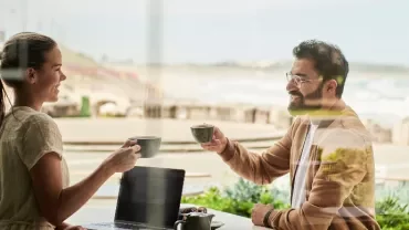 Two people enjoying coffee and conversation at a beachside cafÃ©.