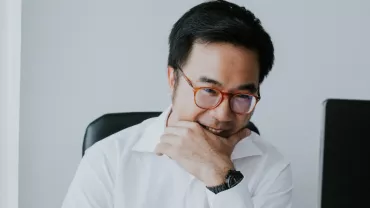 Man in glasses smiling at a desk with two computers.