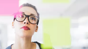 Person with glasses looking at colorful sticky notes on glass.