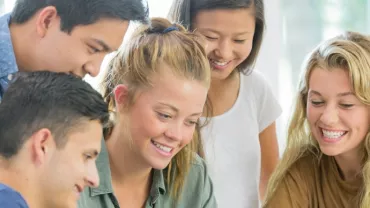 Group of smiling young people looking at a laptop together.