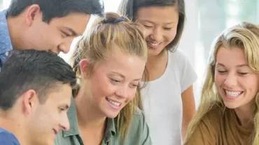 Group of smiling young people looking at a laptop together.