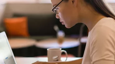 Person with glasses focused on a laptop in a cozy cafe.