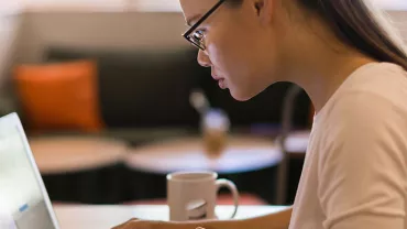 Person with glasses focused on a laptop in a cozy cafe.