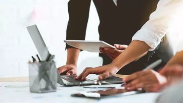 Group of people working together on laptops and tablets at a desk.